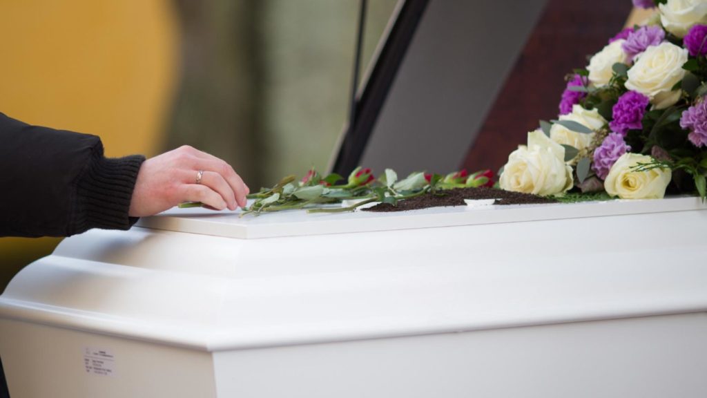 hand placing flowers on a casket