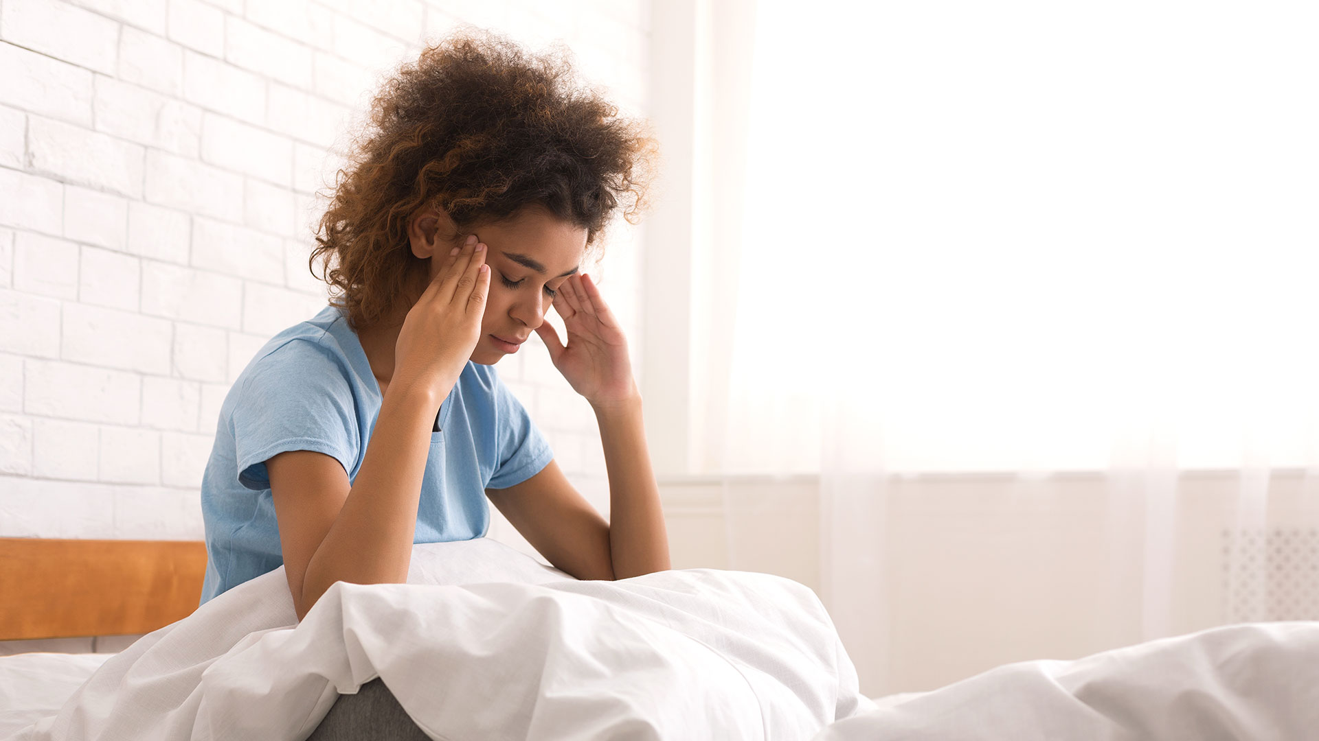 Woman with terrible headache, sitting on bed in the morning